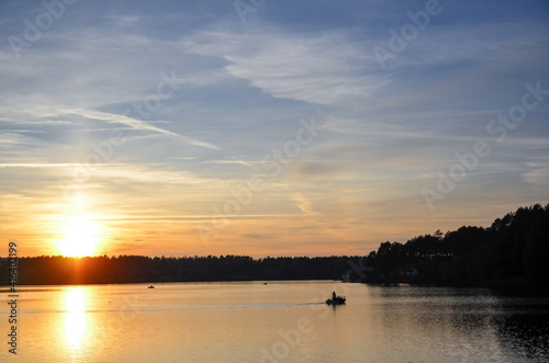 Orange sunset over the lake with silhouette of fisherman boat. Selective focus. © kyrychukvitaliy