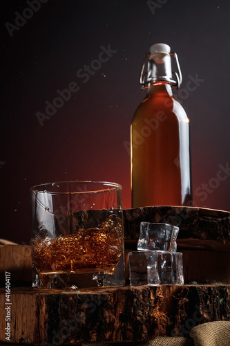 A glass of alcohol near a bottle. Old whiskey bottle on black wooden table. Drinks on a dark blurred background.