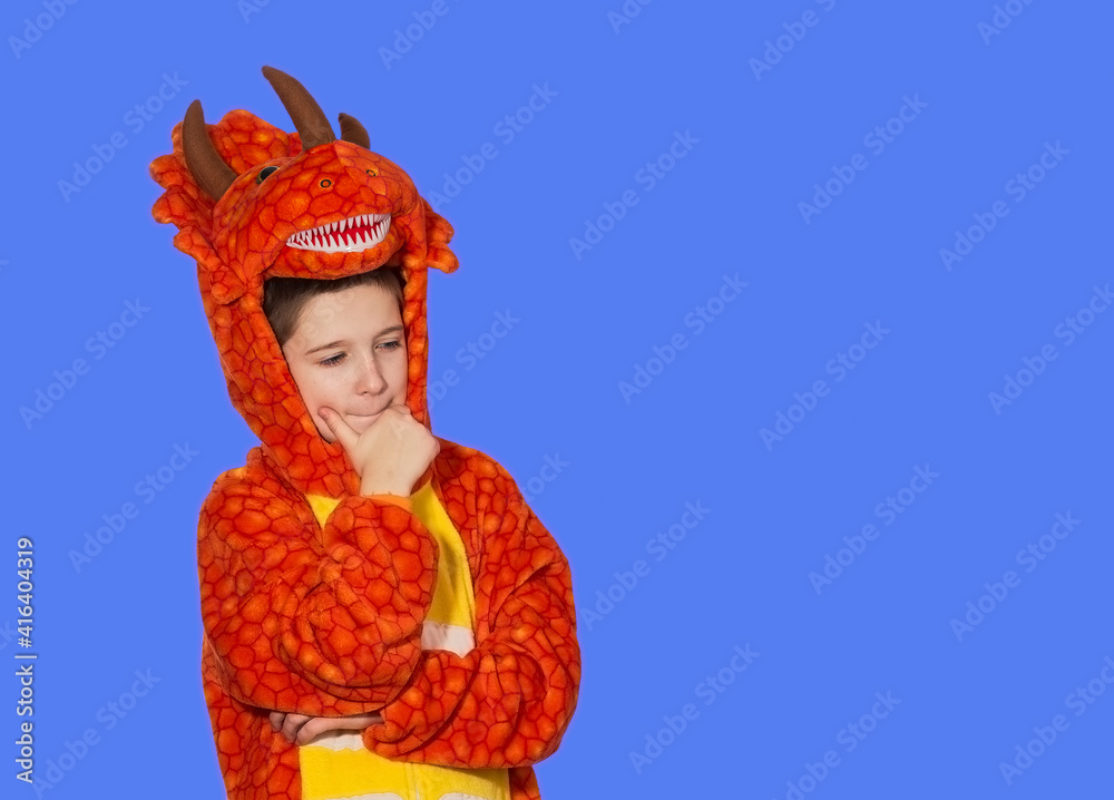 boy in dragon pajamas stands pensive against blue background with copy space
