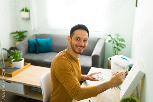 Attractive man smiling while doing a painting on a canvas © AntonioDiaz