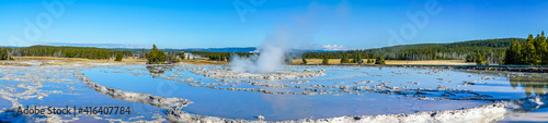 Panorama of circular tiered thermal pools reflecting the clear blue sky with a steaming center building pressure