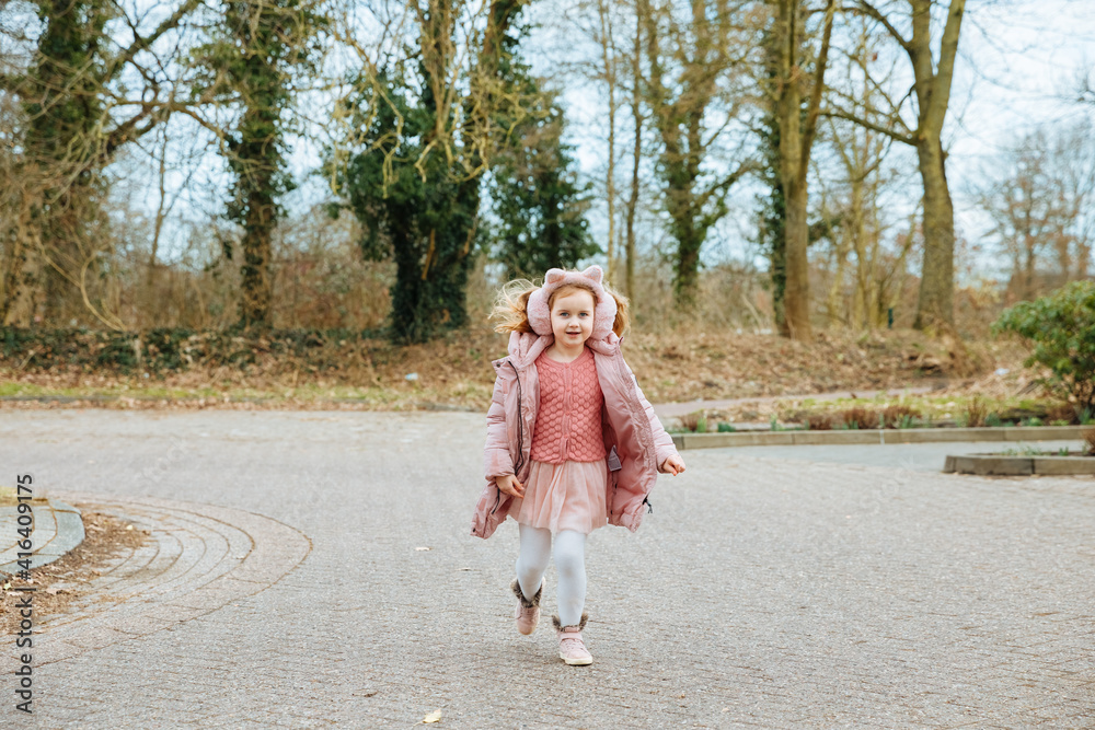 child walking in the park. Little blond girl in thick clothes runs in a paved parking lot. Child is happy to be picked up from kindergarten. Little girl dressed in pink is running and is very happy child walking in the park. Little blond girl in thick clothes runs in a paved parking lot. Child is happy to be picked up from kindergarten. Little girl dressed in pink is running and is very happy