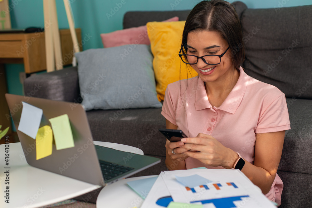 Young businesswoman is working from home on a laptop and typing on her phone. Young businesswoman is working from home on a laptop and typing on her phone.