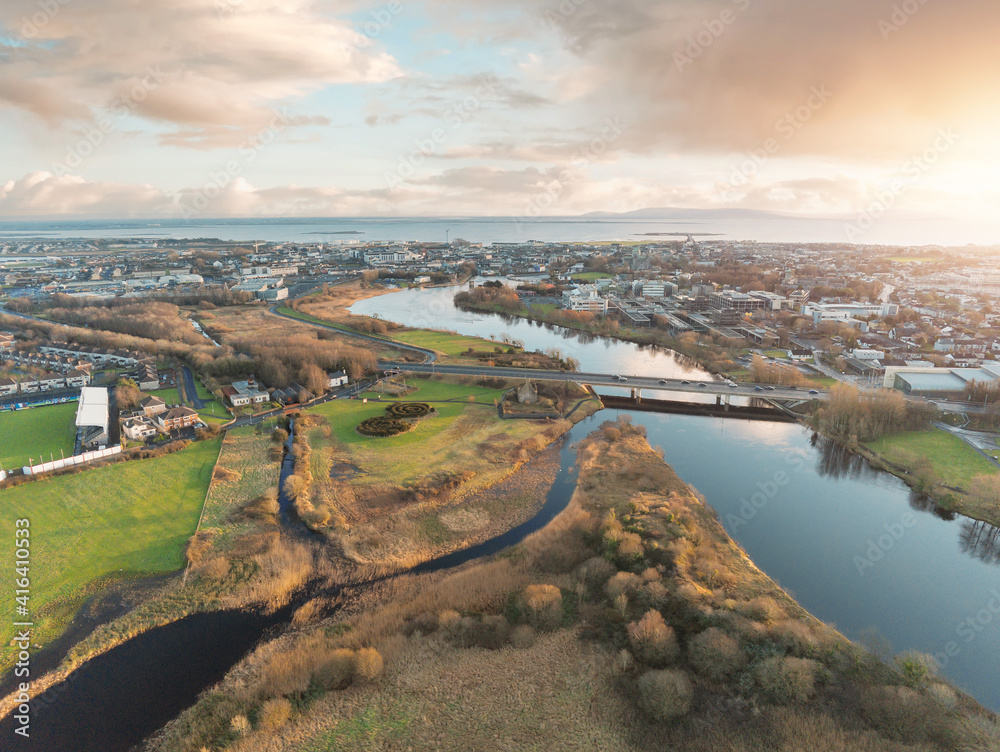 Aerial drone view on Sunset over Galway city, Bridge over River Corrib and NUI buildings, Atlantic ocean in the background. West coast of Ireland. Warm sunny cloudy sky, Sun flare