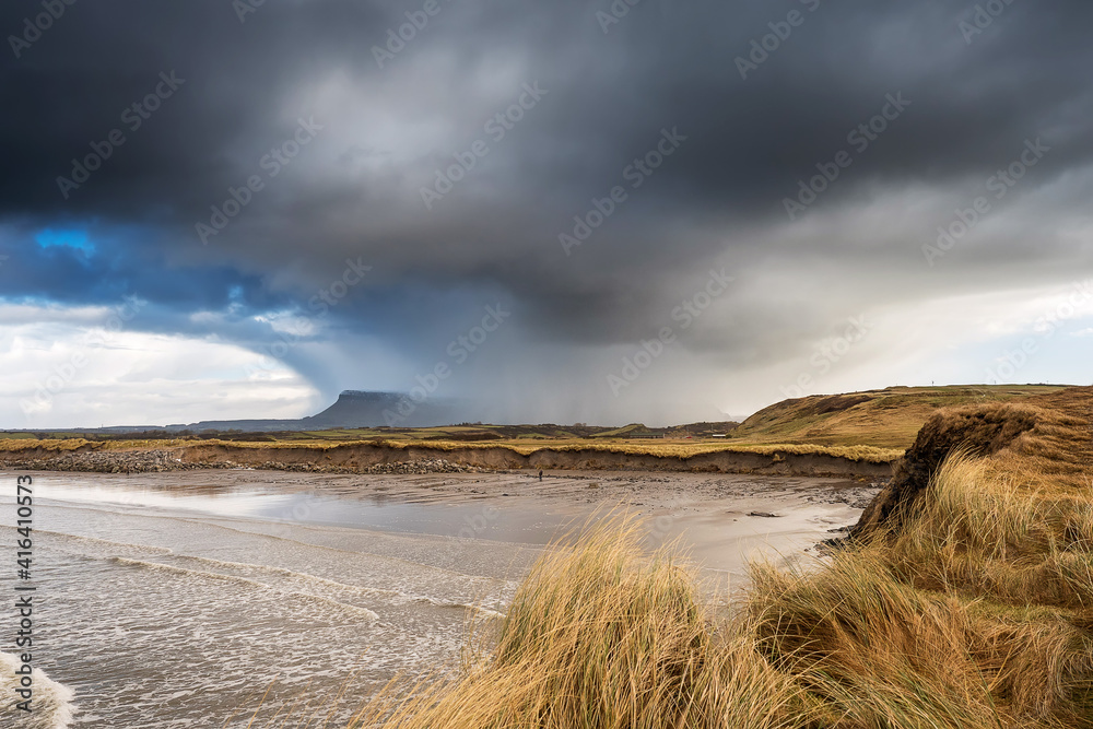 Rosses point beach and Benbulben flat top mountain covered in snow in county Sligo, Ireland, Warm sunny day, cloudy blue sky covers the peak of the mountain.