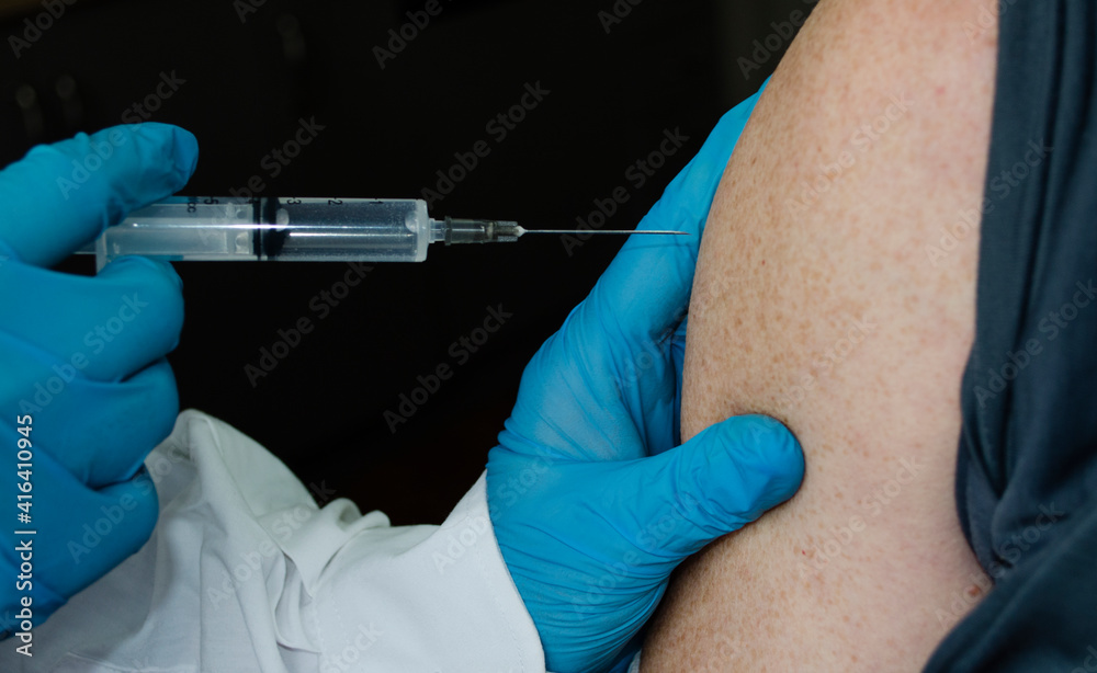 Blurred hands with a syringe injecting the vaccine into the shoulder.Vaccination procedure. Human vaccination process against coronavirus. A selective focus shot of a vaccine injection. Blurred hands with a syringe injecting the vaccine into the shoulder.Vaccination procedure. Human vaccination process against coronavirus. A selective focus shot of a vaccine injection.