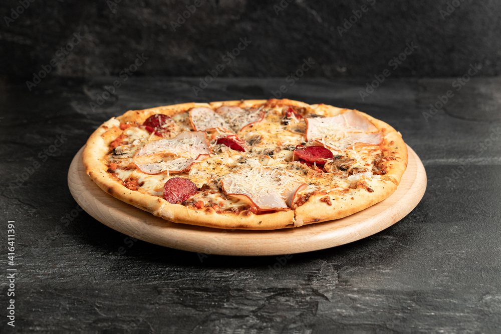 Hot tasty traditional italian pizza with salami, meat, cheese, tomatoes greens on a dark background