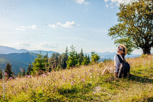 Traveling in summer Ukraine. Trip to Carpathian mountains. Happy woman tourist sitting in flowers after hiking