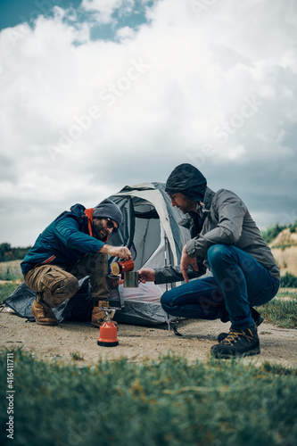 Two campers crouching by the tent and preparing coffee.