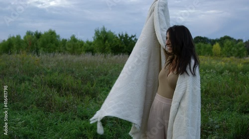 Attractive young adult woman waves to friends in field getting ready for sunset picnic in summer