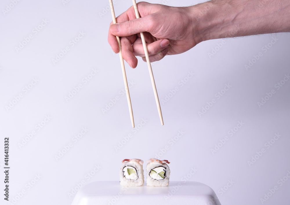 A man's hand reaching out with tasting sushi sticks to a plate of Japanese sushi with rice and vegetables and fish meat on a white background A man's hand reaching out with tasting sushi sticks to a plate of Japanese sushi with rice and vegetables and fish meat on a white background