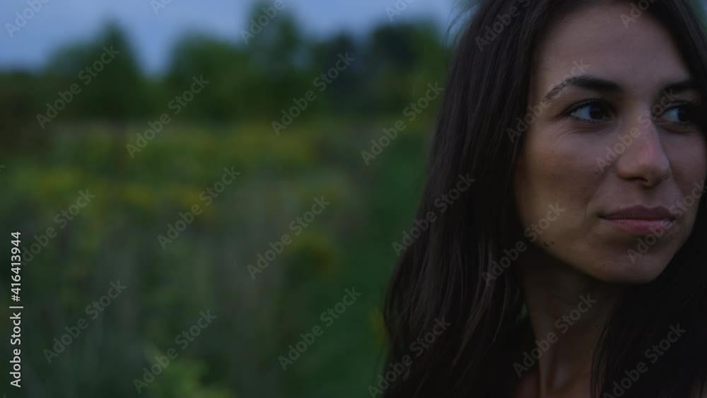 Attractive woman walks through field at sunset in summer - close up on face turning around Attractive woman walks through field at sunset in summer - close up on face turning around