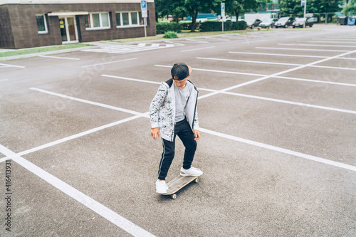 Teenager skateboarder boy riding a skateboard on asphalt playground with white lines doing tricks. Youth generation Freetime spending concept image.