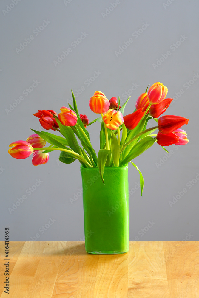 A vase of yellow and orange tulip flowers in a green vase