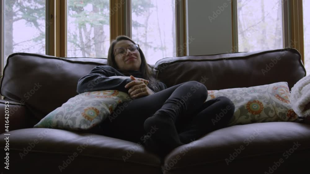 Young adult woman watches tv and laughs at screen while sitting on couch Young adult woman watches tv and laughs at screen while sitting on couch