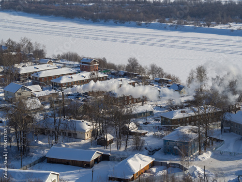 A suburb, village or industrial quarter of a winter city from a bird's-eye view (photo from an aerial drone). Russian backwoods, view on the frozen ice of the river Vyatka.