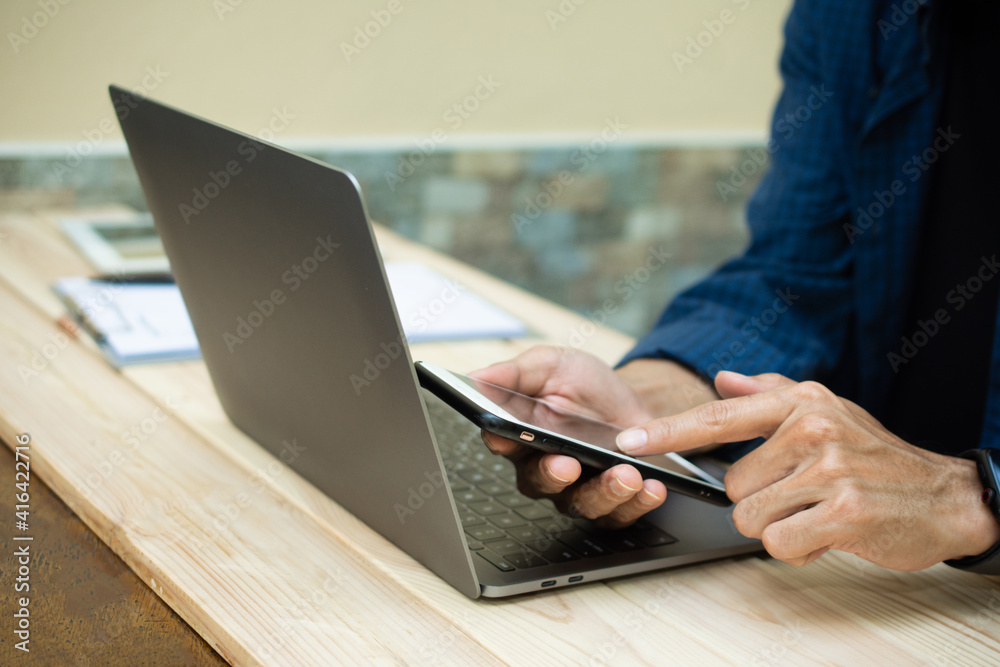 Fototapeta premium Hand using phone with laptop working at home