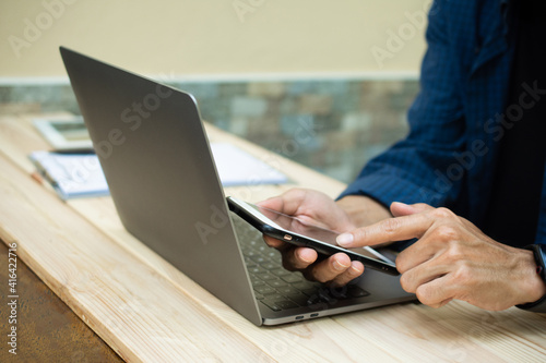 Hand using phone with laptop working at home © Suriyo
