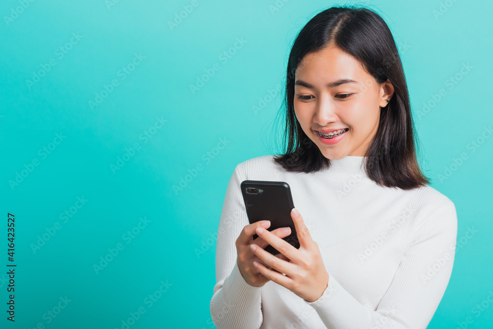 Portrait of Asian woman smile she holding and typing text message on a smartphone, female excited cheerful her reading mobile phone some social media isolated on a blue background, Technology concept Portrait of Asian woman smile she holding and typing text message on a smartphone, female excited cheerful her reading mobile phone some social media isolated on a blue background, Technology concept