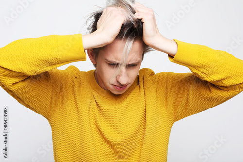 Young handsome man wearing yellow sweater with hand on head, headache because stress. suffering migraine.