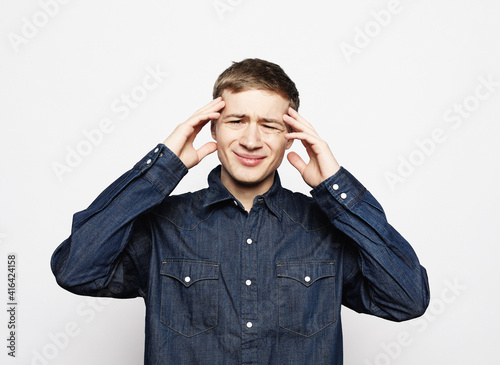 Young handsome man wearing jeans shirt with hand on head, headache because stress. suffering migraine.