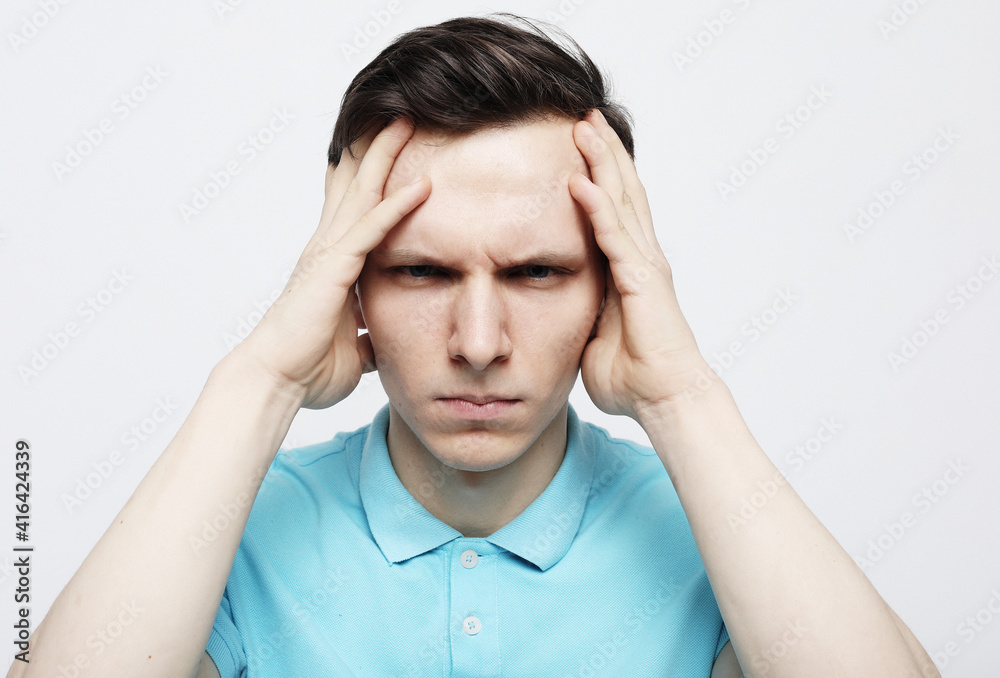 Young handsome man wearing casual blue t-shirt over white isolated background with hand on head for pain in head because stress. Young handsome man wearing casual blue t-shirt over white isolated background with hand on head for pain in head because stress.