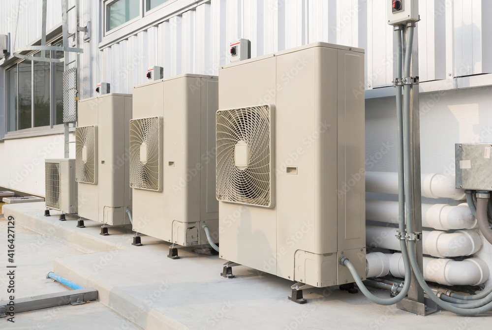 Condenser unit or compressor outside industrial plant building. Unit of central air conditioner (AC) or heating ventilation air conditioning system (HVAC). Electric fan and refrigerant pump inside. Condenser unit or compressor outside industrial plant building. Unit of central air conditioner (AC) or heating ventilation air conditioning system (HVAC). Electric fan and refrigerant pump inside.