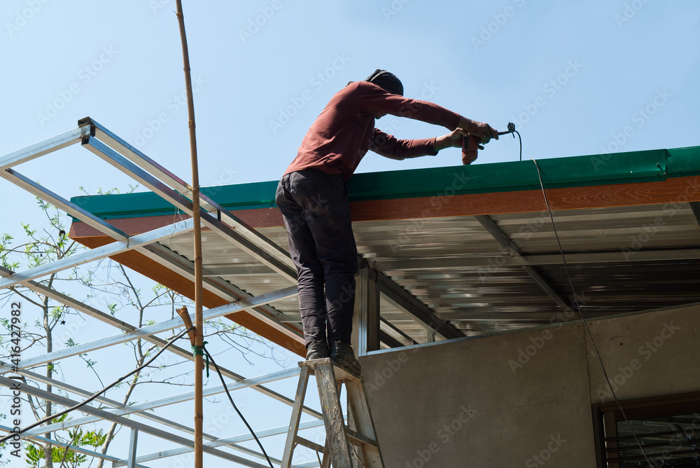 Unsafe Male Roofer Workman Using Electric Screwdriver Install Tile on Roof of New House in the Construction Site with no Protection.