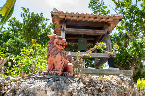 Shisa, a traditional decoration from the Ryukyu Kingdom, Okinawa used for protection and behind it the traditional Japanese temple bell. Taketomi Island.