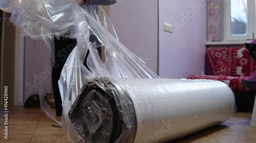 A grown man unpacks a new mattress. Unpacking the mattress with a knife pressed into the bag