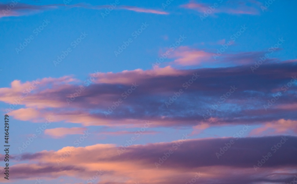 This image showcases whimsical fluffy sunset clouds in a bright blue sky