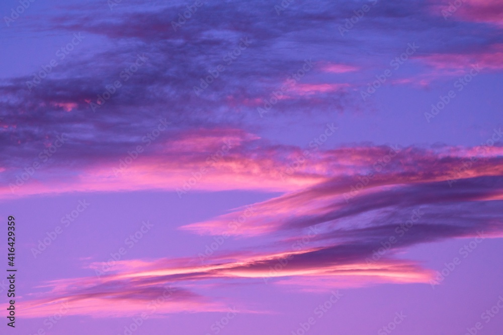 This image features an idyllic calm sky filled with pink and purple clouds illuminated by a stunning sunset.