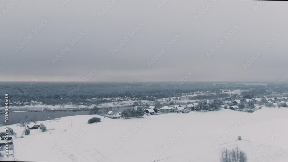 Ascending aerial drone view of little village near river and forest in background, winter. Ascending aerial drone view of little village near river and forest in background, winter.