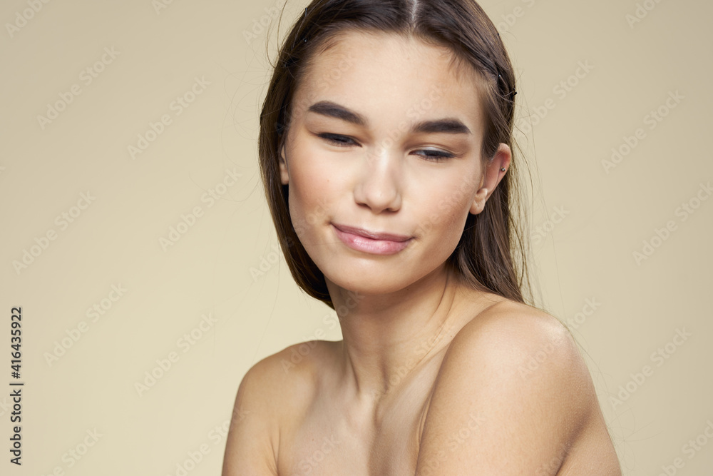 Brunette with bare shoulders close-up long hair beige background clean skin Brunette with bare shoulders close-up long hair beige background clean skin