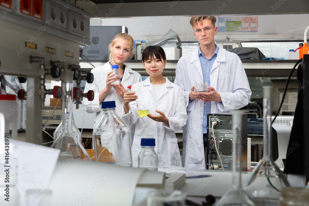 Obraz premium Glad male and female scientists in white coats posing at biochemical laboratory