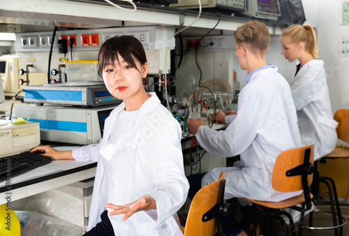 Young efficient glad smiling Chinese female student posing near equipment at laboratory