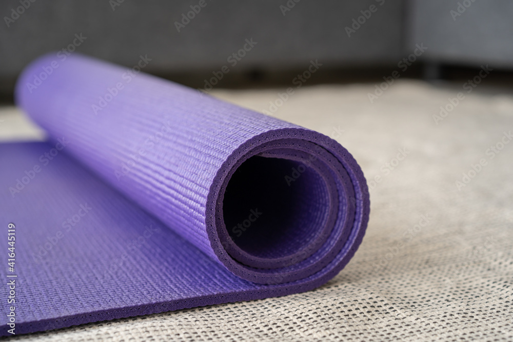 Rolled purple yoga exercise mat on the floor in living room close up with copyspace. Indoor workout activity concept. Rolling Purple Yoga carpet close up.