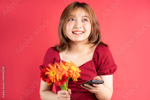 Young girl holding flowers and using phone with cheerful expression on background