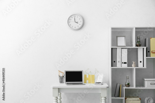 Modern comfortable workplace with laptop near light wall in office © Pixel-Shot