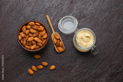 Jar with almond flour and bowl of nuts on dark background