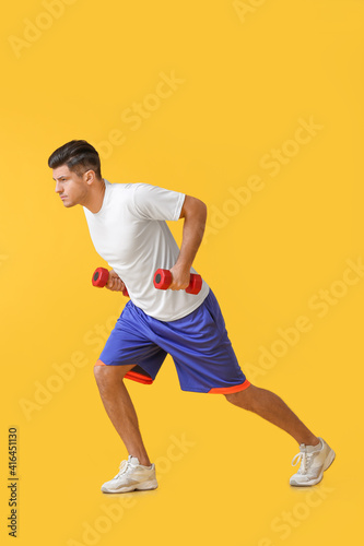 Sporty young man training with dumbbells on color background © Pixel-Shot