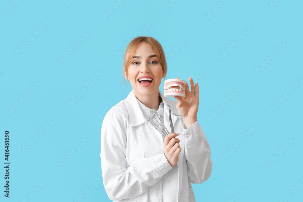 Female dentist with plastic jaw model and tools on color background Female dentist with plastic jaw model and tools on color background