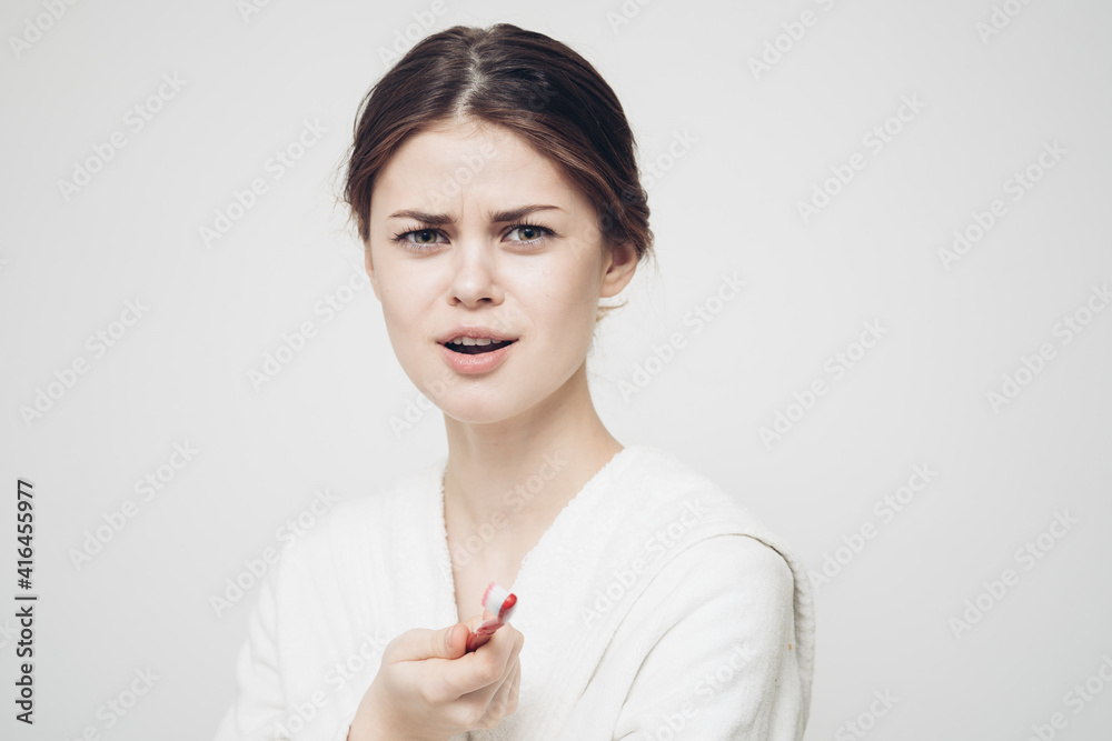 emotional woman with a toothbrush in her hand on a light background and a white robe side view emotional woman with a toothbrush in her hand on a light background and a white robe side view