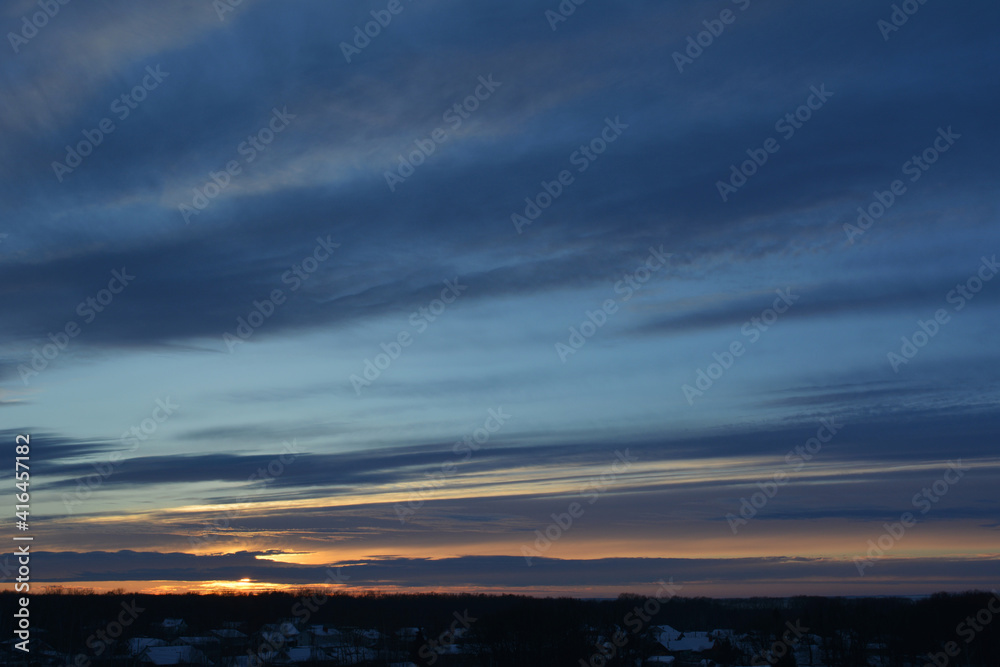 Landscape with sunset at winter. Dark blue striped clouds on the sky