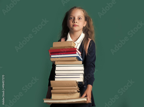 Funny Kid. Back to school and homework concept. Schoolgirl with shocked face holds huge pile of books.