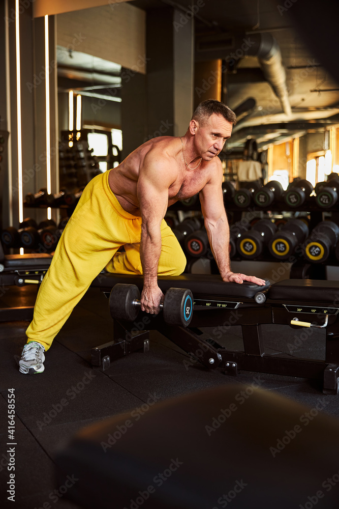 Naklejka premium Professional fitness coach doinf exercises with bench and dumbbells