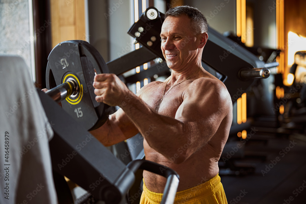 Obraz premium Positive male athlete adjusting a weight for a barbell