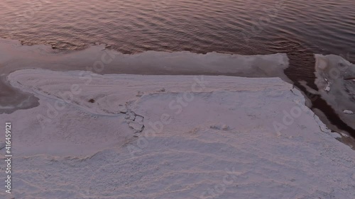 Aerial view over partialy frozen sea and small river delta. White frozen waves ice texture from above shot with drone.