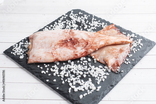 Raw squid carcass with spices and coarse salt on a black slate board. copy space Top view. photo