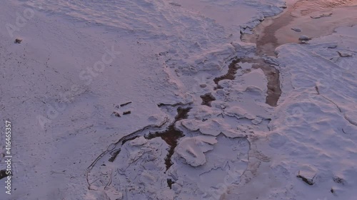Aerial view over partialy frozen sea and small river delta. White frozen waves ice texture from above shot with drone.